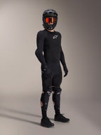 Alpinestars A-Impact Plasma Pro knæ- og skinnebensbeskyttere, sort og hvid, båret af en rytter med et komplet mountainbike-beskyttelsessæt, herunder en sort langærmet beskyttelsesoverdel, sorte handsker og en full-face hjelm med orange goggles.