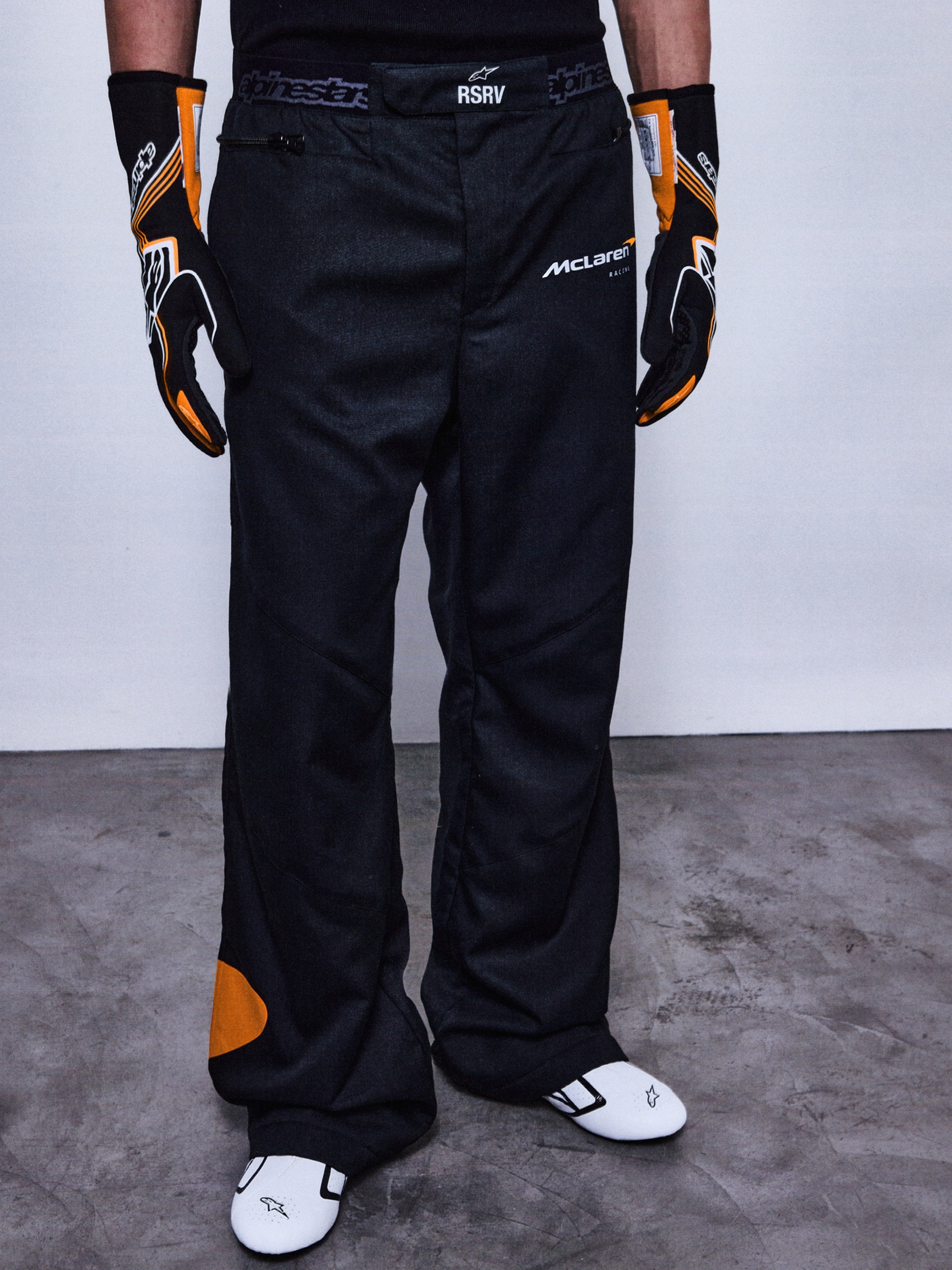 Alpinestars RSRV Arena Suit bukser, racerbukser til motorcykel, sort med orange detaljer, McLaren-logoer, premium beskyttelsesudstyr, vist med matchende handsker og racerstøvler