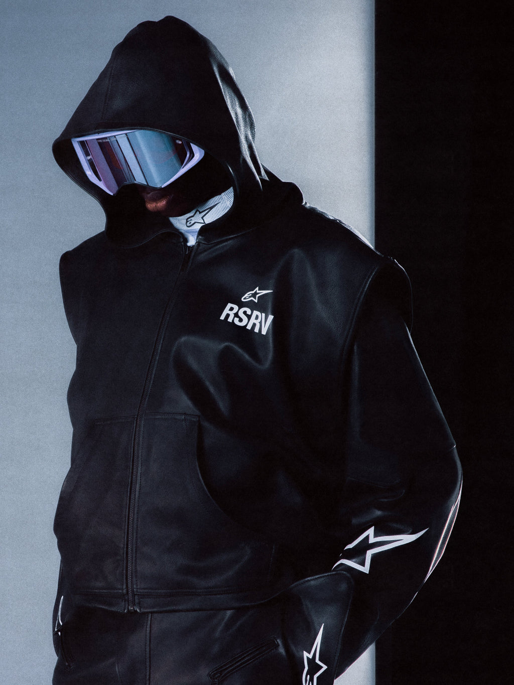 Alpinestars RSRV Axis læderhættetrøje, sort premium læderjakke med hætte, unisex streetwear, hvide stjerne-detaljer på ærmerne, RSRV-logo på brystet, futuristisk design, glat lædertekstur