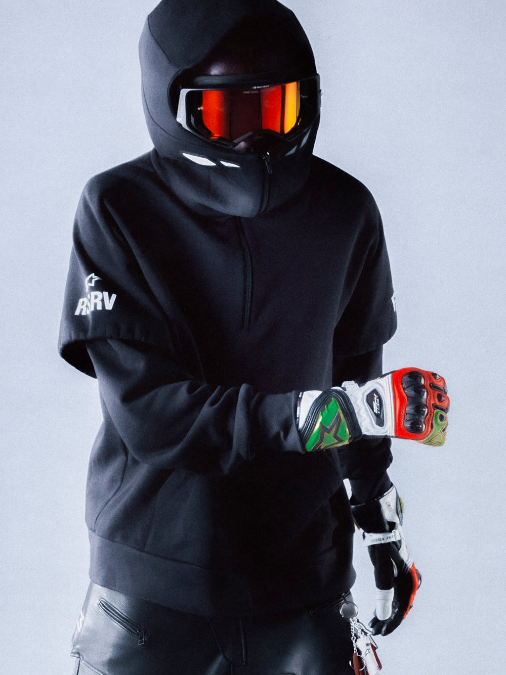 Alpinestars RSRV Vault Hoodie, sort hættetrøje, person iført motorcykelhjelm med reflekterende rød-orange visir, farverige handsker, sort beskyttelsesudstyr, moderne streetwear design med hvide logoer på ærmet