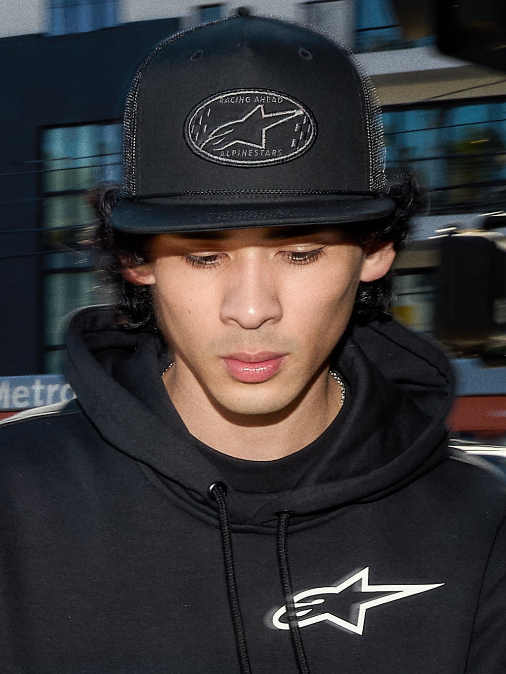 Alpinestars Contender Trucker Hat, sort lifestyle-kasket med poly mesh-bagside, struktureret krone med et broderet Astars logo-mærke, bæres af en mand med en sort Alpinestars hættetrøje, afslappet motorsport-inspireret streetwear.