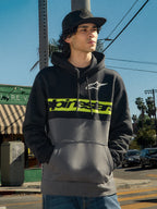 Alpinestars Parallel hættetrøje, lifestyle streetwear, farveblokket sort og gunmetal design, limegrøn bryststribe med Alpinestars-logo, hvidt Astars-logo, hætte med snøre, båret af en mand i et udendørs bymiljø