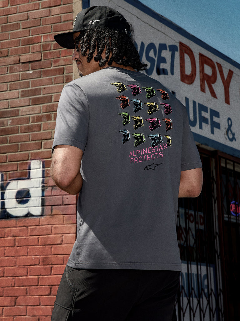 Alpinestars Pop Helmet CSF Tee, kortærmet t-shirt, koksgrå, grafik på ryggen med farverige M10-hjelme og pink "ALPINESTAR PROTECTS" tekst, afslappet motorsport-inspireret streetwear
