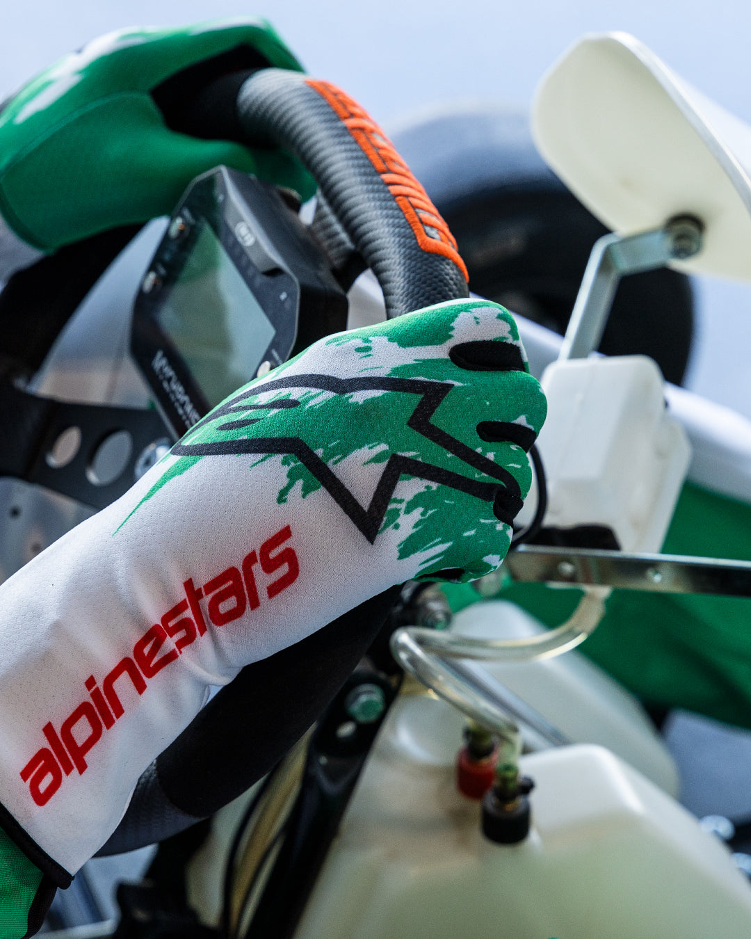 Alpinestars Tech-1 K V3 handsker i hvid, grøn og rød, førerens hænder der griber om et gokart-rat, med grønt sublimeret splash-design, sort stjerne-logo og rød Alpinestars-tekst på manchetten, professionelt gokart-udstyr