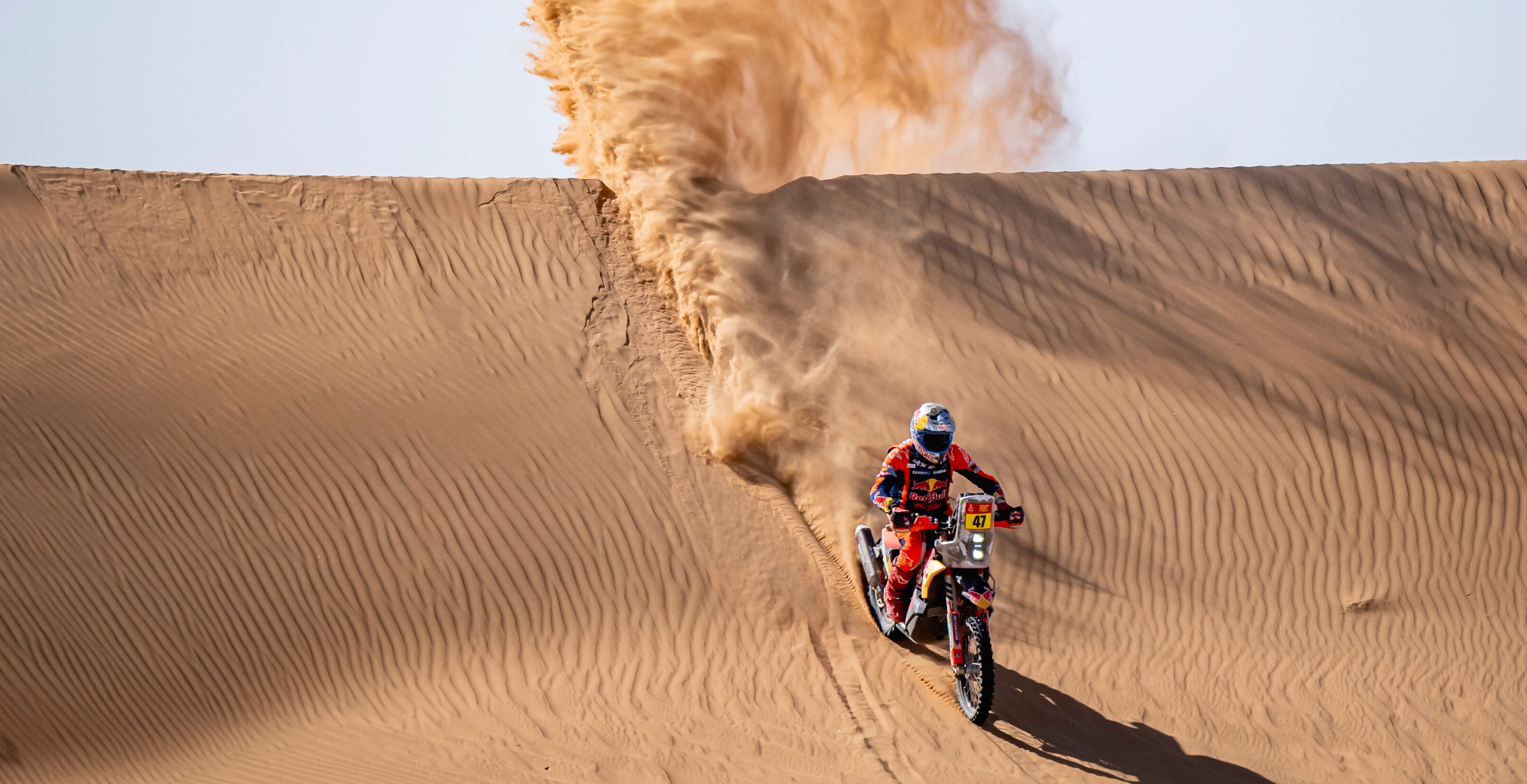 Kevin Benavides riding a rally motorbike on sand dunes with a large cloud of dust behind