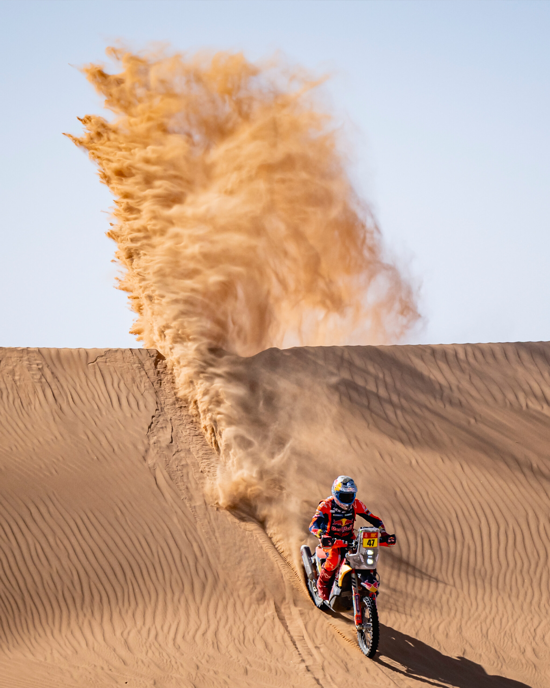 Kevin Benavides riding a rally motorbike on sand dunes with a large cloud of dust behind