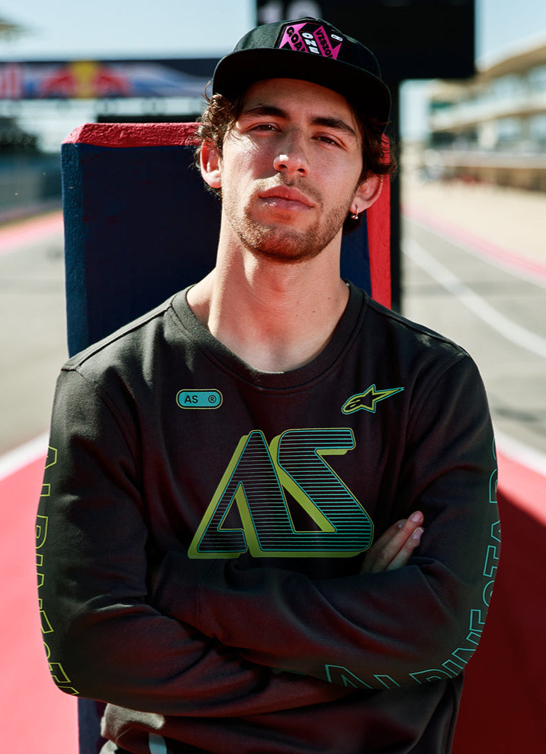 Alpinestars Ayess Csf Tee, langærmet t-shirt, sort, med grøn og gul gradient AS-grafik på brystet og ærmerne, afslappet motorsport-inspireret streetwear, båret på en racerbane