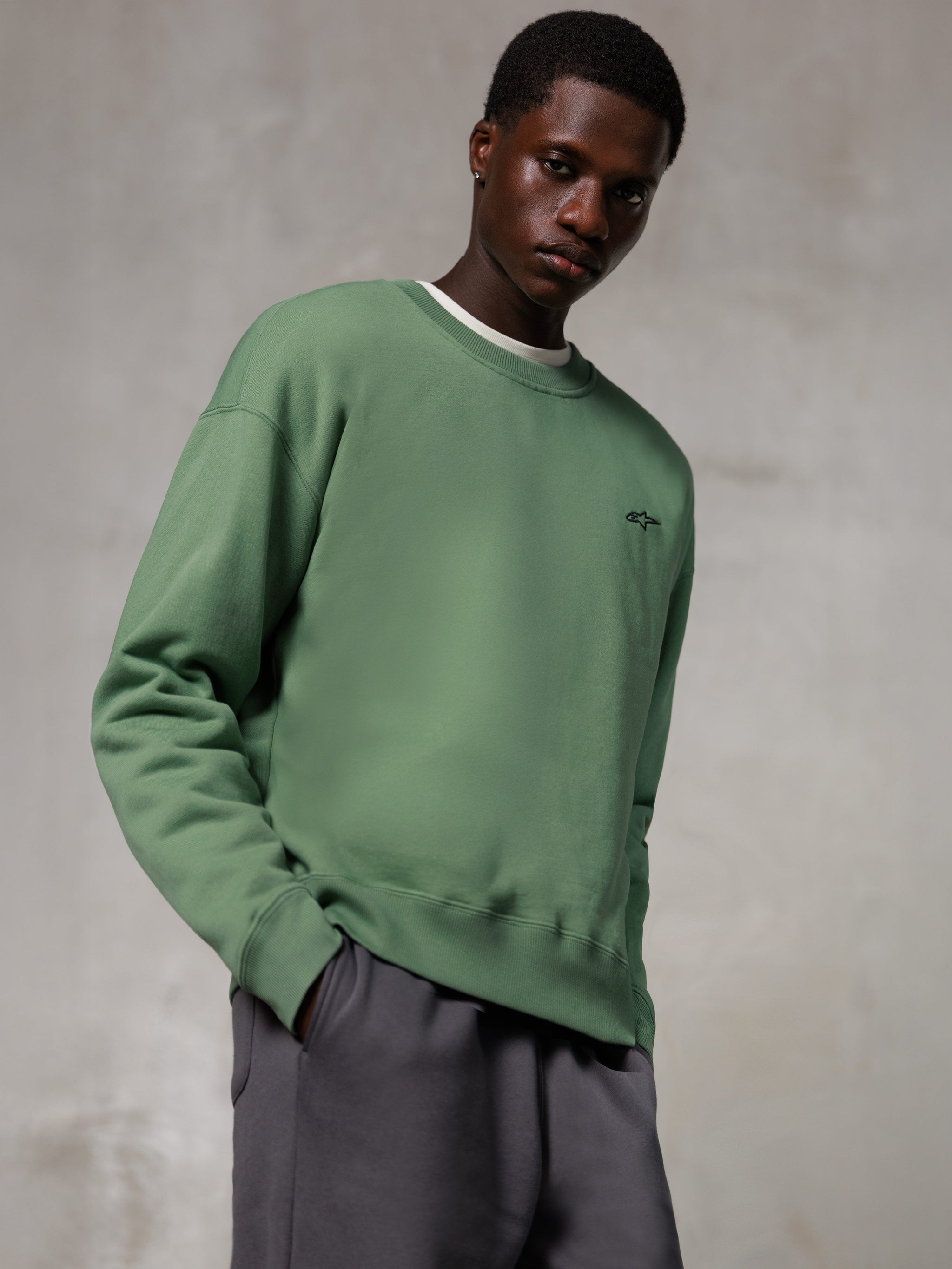 Alpinestars Essentials Ageless Crew, crewneck sweatshirt, kaktusgrøn, med et lille sort Alpinestars-logo på brystet, båret af en model med grå bukser, afslappet lifestyle streetwear