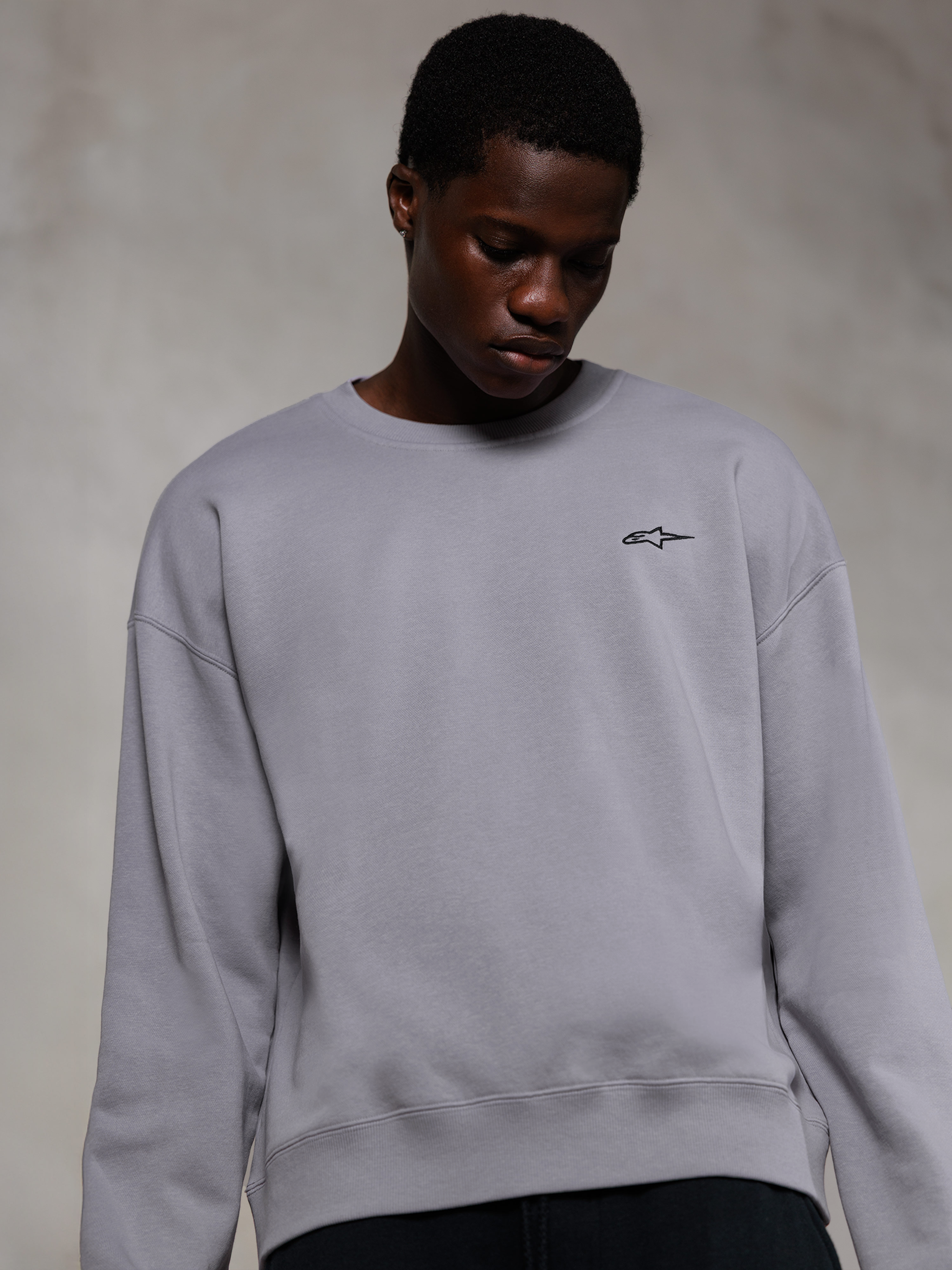 Alpinestars Essentials Ageless Crew, sølvfarvet premium crewneck sweatshirt, med et lille sort Alpinestars-logo på brystet, båret af en model, afslappet lifestyle streetwear med en blød fleecetekstur.