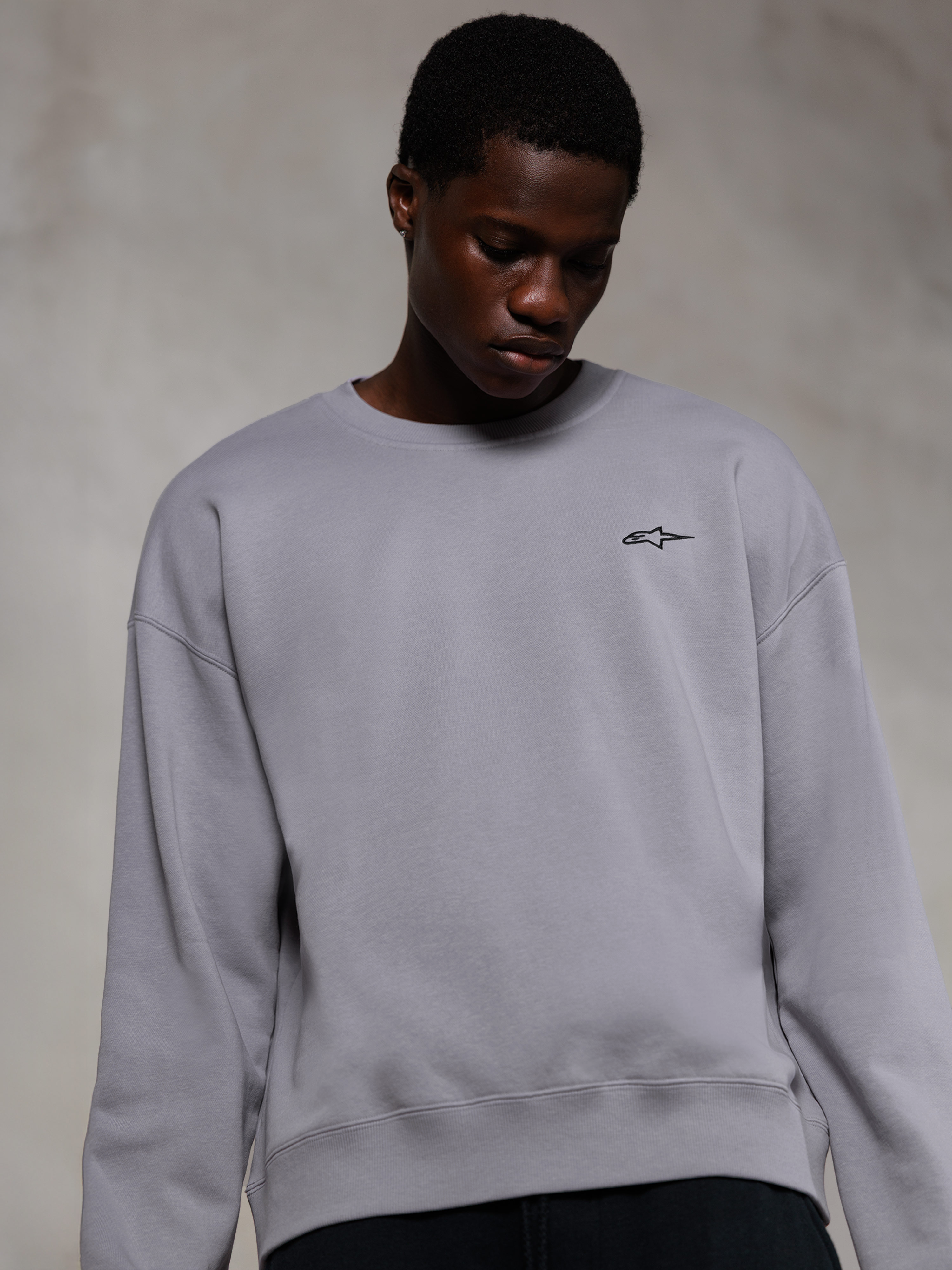 Alpinestars Essentials Ageless Crew, sølvfarvet premium crewneck sweatshirt, med et lille sort Alpinestars-logo på brystet, båret af en model, afslappet lifestyle streetwear med en blød fleecetekstur.