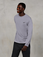 Alpinestars Essentials Ageless LS Tee, langærmet t-shirt, sølv, lille sort logo på brystet, båret af en smilende model med mørke bukser, afslappet moderne pasform, afslappet motorsport-livsstilstøj