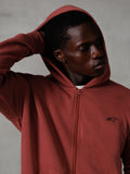 Alpinestars Essentials Ageless Zip Hættetrøje, teglrød, afslappet lifestyle streetwear, hætte oppe med hånd bag hovedet, lille sort Astars-logo på brystet, fleecehættetrøje med afslappet pasform