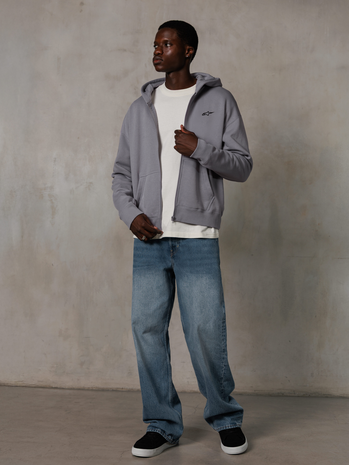 Alpinestars Essentials Ageless Zip Hoodie, Silver, afslappet streetwear, fleece-hættetrøje med fuld lynlås og et lille sort logo på brystet, båret af en model med en hvid t-shirt og blå jeans, afslappet lifestyle-pasform