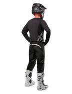 Alpinestars 2024 Fluid Graphite-gearsæt, motocross-kører set bagfra, grafitgrå jersey og bukser med sølvfarvet Alpinestars-branding, sort hjelm og hvide motocross-støvler, udstyr med atletisk pasform til off-road-kørsel
