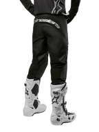 Alpinestars 2024 Fluid Graphite-udstyrssæt, set bagfra af sorte og grå motocrossbukser med hvidt Alpinestars-branding på bagdelen, båret med hvide og sorte motocross-støvler, specialiseret off-road-racerudstyr