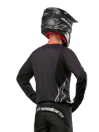 Alpinestars 2024 Fluid Graphite udstyrssæt, motocross-trøje og bukser, grafit og sølv, set bagfra med sølvfarvet branding på lænden og i taljen, båret med sort hjelm med kulfibereffekt, letvægtsdesign i poly-stof til terrænkørsel