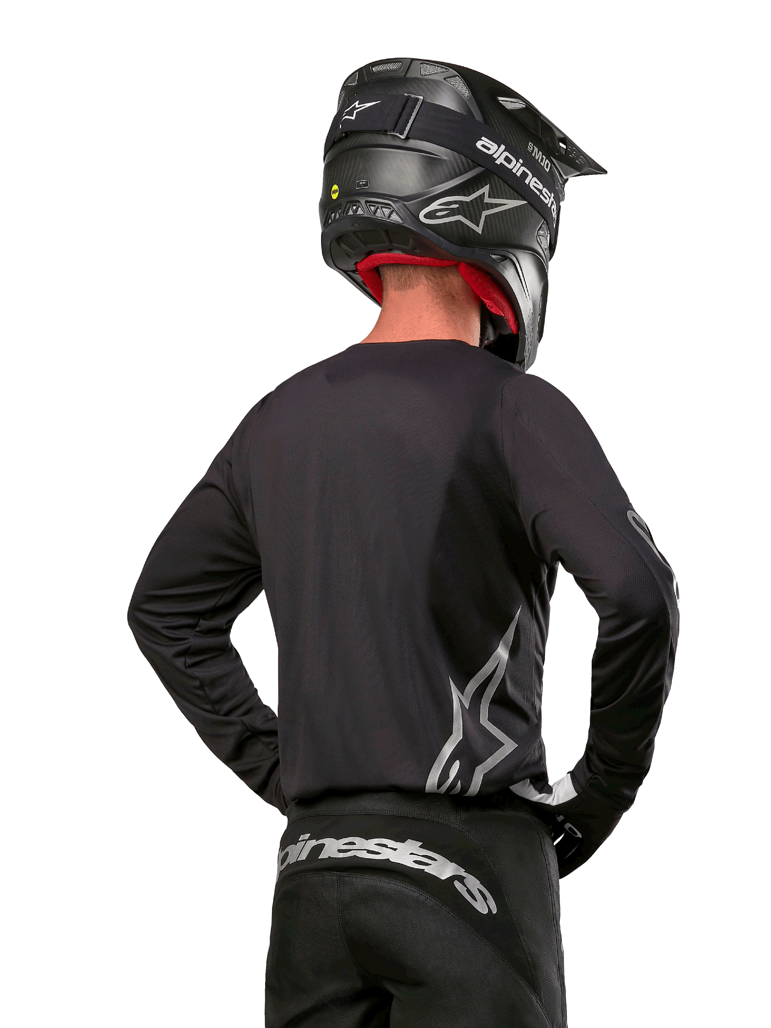 Alpinestars 2024 Fluid Graphite udstyrssæt, motocross-trøje og bukser, grafit og sølv, set bagfra med sølvfarvet branding på lænden og i taljen, båret med sort hjelm med kulfibereffekt, letvægtsdesign i poly-stof til terrænkørsel