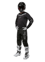 Alpinestars 2024 Fluid Graphite-udstyrssæt, komplet motocross-raceroutfit, sort med grå og hvide logoer, bestående af trøje og bukser båret med matchende sort hjelm, hvide og sorte handsker og støvler, designet til off-road beskyttelse
