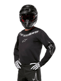 Alpinestars 2024 Fluid Graphite Jersey, Black and Silver Motocross Jersey, long-sleeve performance fit, worn with a black helmet and white gloves, featuring silver Alpinestars branding, off-road racing gear