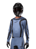 Motocross-rytter iført Alpinestars 2024 Fluid Lurv-trøje, lyseblå og sort, kombineret med sort hjelm og goggles, med markante sorte grafiske detaljer og Alpinestars-stjernelogo, atletisk performance-udstyr til off-road racing