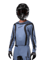 Motocross-rytter iført Alpinestars 2024 Fluid Lurv-trøje, lyseblå og sort, kombineret med sort hjelm og goggles, med markante sorte grafiske detaljer og Alpinestars-stjernelogo, atletisk performance-udstyr til off-road racing