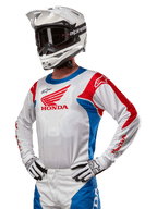Motocrosskører iført Honda Racer Iconic Jersey i hvid, klar blå og klar rød, med et stort Honda-vingelogo på brystet, kombineret med hvid Alpinestars-hjelm og matchende hvide og sorte handsker, koordineret udstyr til terrænkørsel