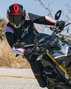 Motorcyklist i et sving på en naked sport motorcykel, Alpinestars T-SPS Air v2-jakke, sort med hvide og røde fluo-detaljer, sort og rød hjelm, sorte handsker, præstationsorienteret tekstiludstyr til urban sportskørsel