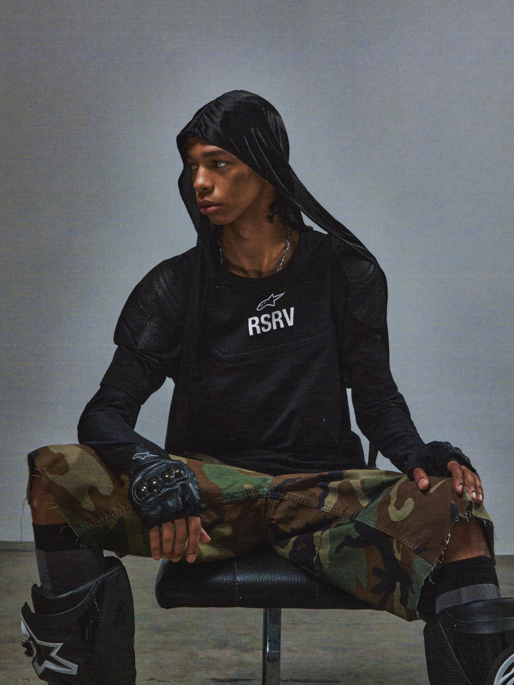 Alpinestars RSRV Nucleon kortærmet t-shirt, sort med hvidt RSRV-logo, unisex streetwear, vist med camouflage bukser og beskyttelsesudstyr, urban motorsport stil