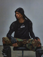 Alpinestars RSRV Nucleon kortærmet t-shirt, sort med hvidt RSRV-logo, unisex streetwear, vist med camouflage bukser og beskyttelsesudstyr, urban motorsport stil