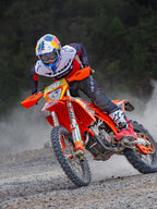 Motocross-rytter i aktion iført Alpinestars Pro-Dura Jersey i sort, rød og hvid, kører på en orange motocross-cykel på en støvet off-road-sti, kombineret med sorte bukser og rød-hvide støvler