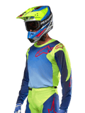 Alpinestars 2024 Racer Hoen Jersey, motocross trøje, neongul og mørkeblå med røde logoer, båret med en matchende gul, blå og rød hjelm og blå handsker, iøjnefaldende udstyr til terrænkørsel