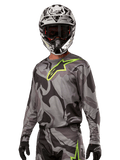 Alpinestars 2024 Racer Tactical Jersey, motocross trøje, Cast Gray Camo Magnet med neongrønt logo, båret med sort og hvid hjelm og sorte handsker, teknisk svedtransporterende materiale til terrænkørsel