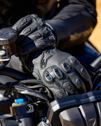 Alpinestars SP X 7 handsker, sorte motorcykelhandsker i perforeret læder med TPU-knobeskyttelse og fingerslidere, vist på en kørers hænder på et motorcykelstyr.