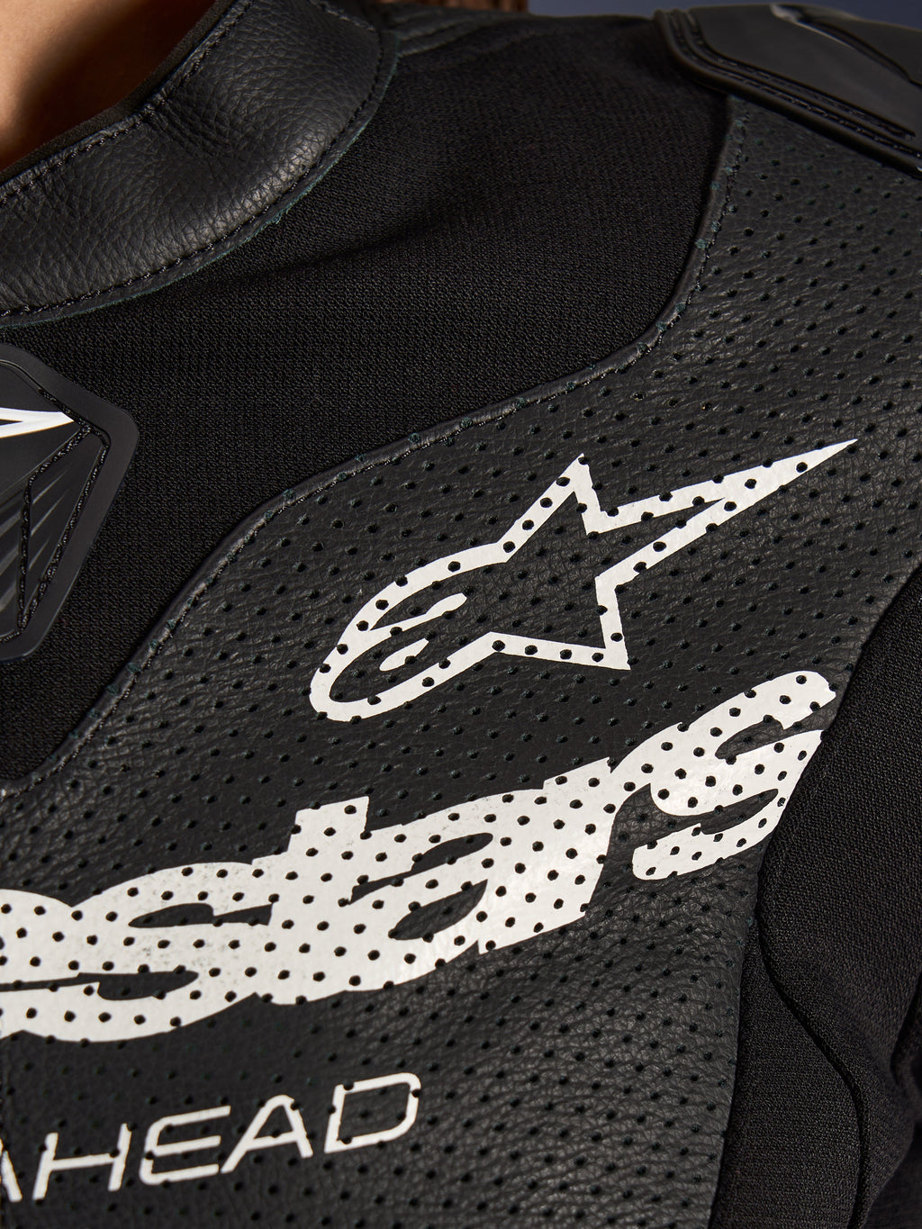 Nærbillede af Alpinestars Stella GP-R7 2-delt læderdragt i sort, med perforerede læderpaneler, et stort hvidt Alpinestars-logo på brystet og åndbare sektioner i strækstof.