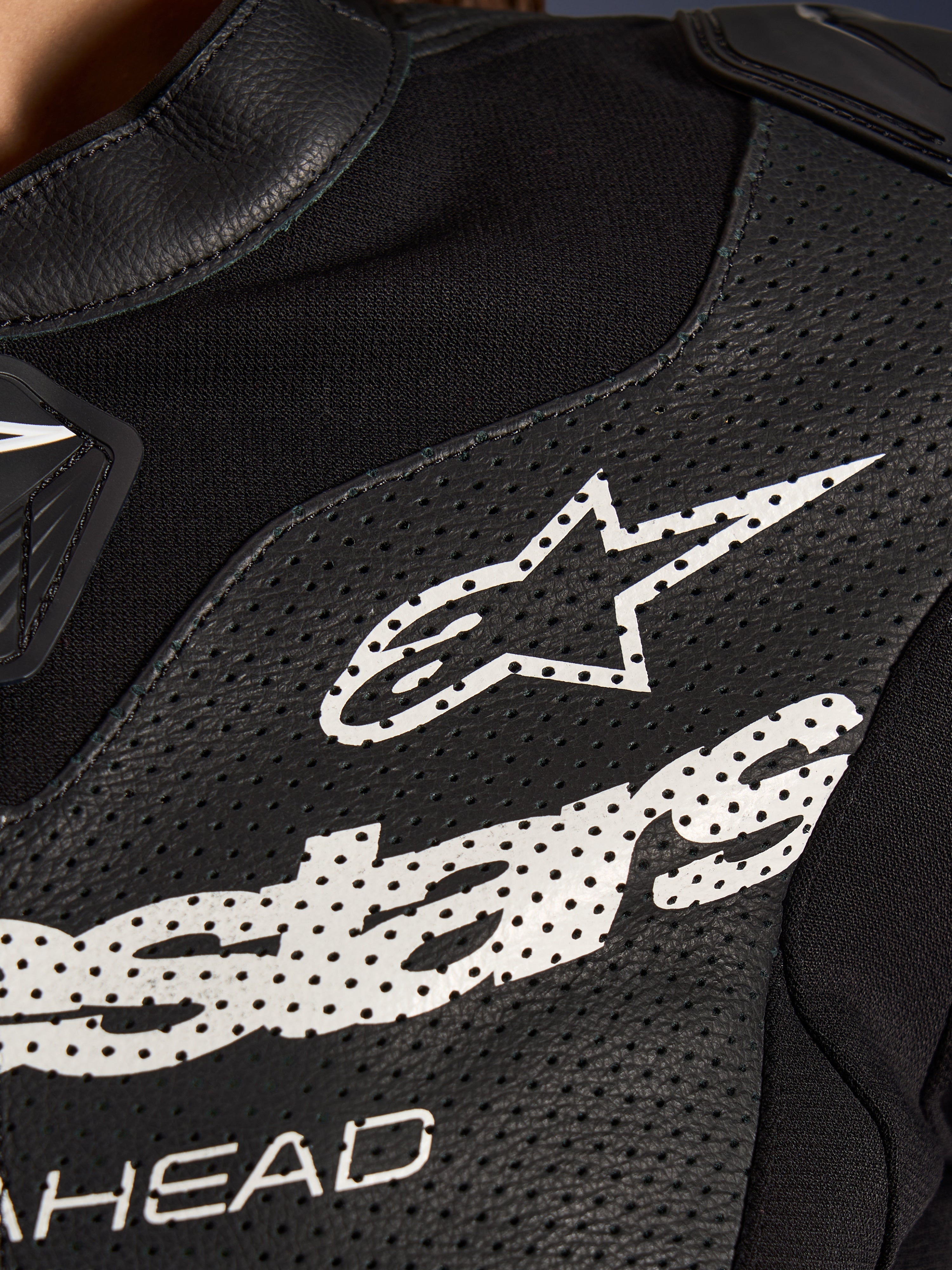 Nærbillede af Alpinestars Stella GP-R7 2-delt læderdragt i sort, med perforerede læderpaneler, et stort hvidt Alpinestars-logo på brystet og åndbare sektioner i strækstof.