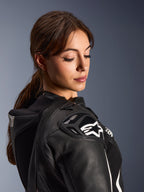 Kvinde iført Alpinestars Stella GP-R7 2-delt læderdragt, nærbillede af sort læderskulder med DFS RR-beskyttelse og hvidt stjernelogo, integreret aero-pukkel og perforerede detaljer.
