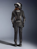 Alpinestars Stella GP-R7 2-delt læderdragt til kvinder, sort med hvide detaljer, set bagfra som viser Supertech R10 aero-pukkel og Tech-Air Ready-logo, båret med matchende full-face hjelm, racerhandsker og læderstøvler til bane- og sportskørsel