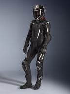 Alpinestars Stella GP-R7 2-delt læderdragt, motorcykeldragt til kvinder, sort med hvide detaljer, båret af en kvindelig kører med en full-face racerhjelm, sorte handsker og støvler, med perforerede læderpaneler og hvid Alpinestars-branding, professionelt racer- og sportsudstyr