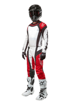 Motocross-rytter iført komplet Alpinestars-udstyr, 2024 Techstar Ocuri-bukser i Mars Red White Black, matchende jersey, sort hjelm med goggles, sort-hvide handsker og hvide motocross-støvler, professionelt off-road raceroutfit