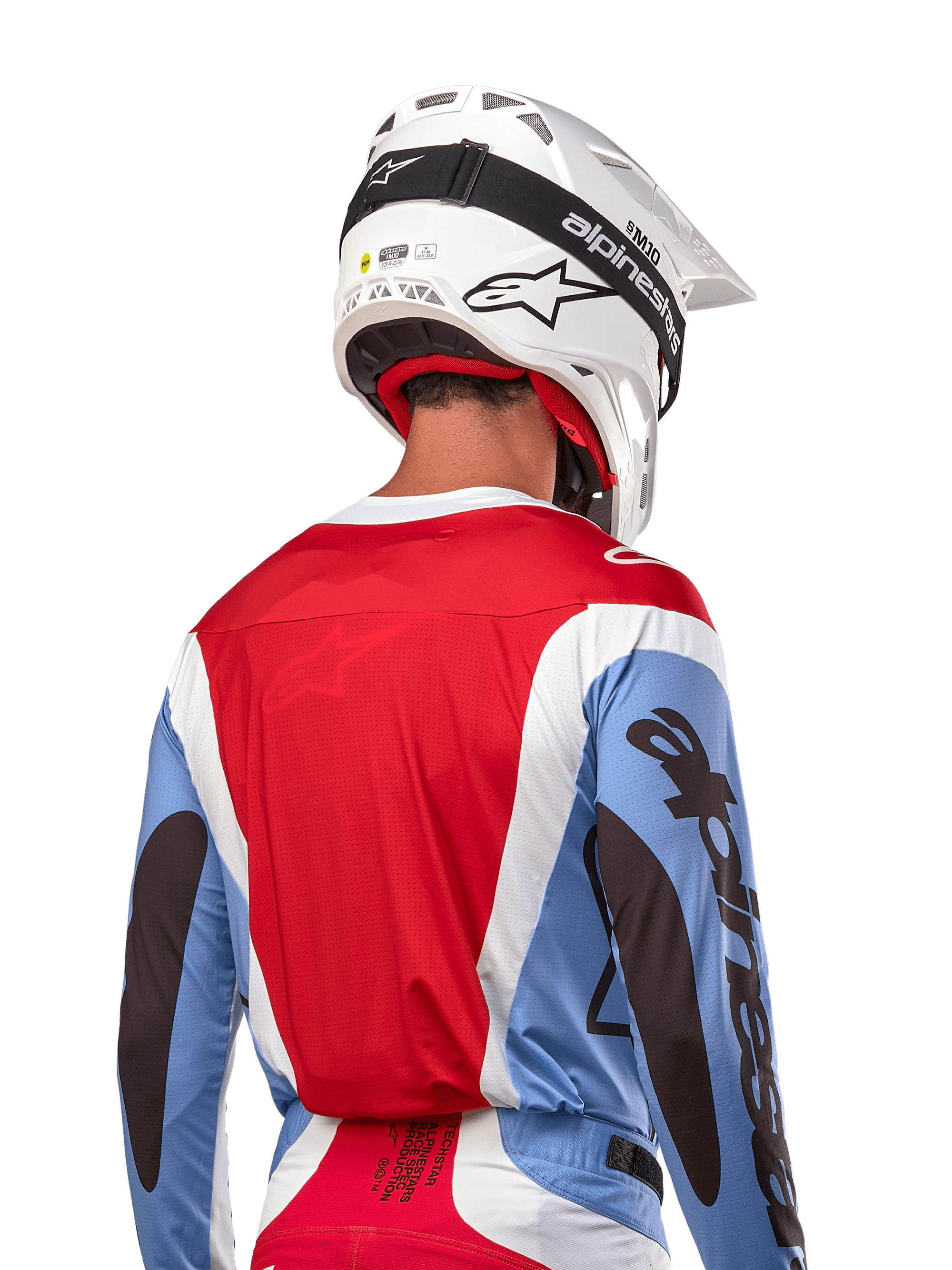 Alpinestars 2024 Techstar Ocuri trøje, motocross-trøje, lyseblå, mars-rød og hvid, set bagfra af kører med matchende hvid hjelm og sorte briller, har markant sort branding på ærmerne og ergonomisk race-pasform til off-road-præstationer