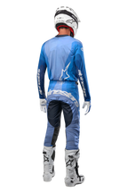 Motocrossrytter set bagfra iført Alpinestars 2024 Techstar Pneuma bukser i mørkeblå og lyseblå, matchende blå trøje, hvid hjelm, hvide handsker og hvide støvler, med tydelig Alpinestars-branding på sædet og ærmerne.