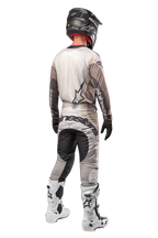 Alpinestars 2024 Techstar Pneuma bukser, motocross-bukser, Dark Sand og Iron Dust Gray, set bagfra båret af en kører med en matchende jersey, hvide og sorte støvler og en sort hjelm, med markant Alpinestars-branding på sædet og forstærkede mørke paneler