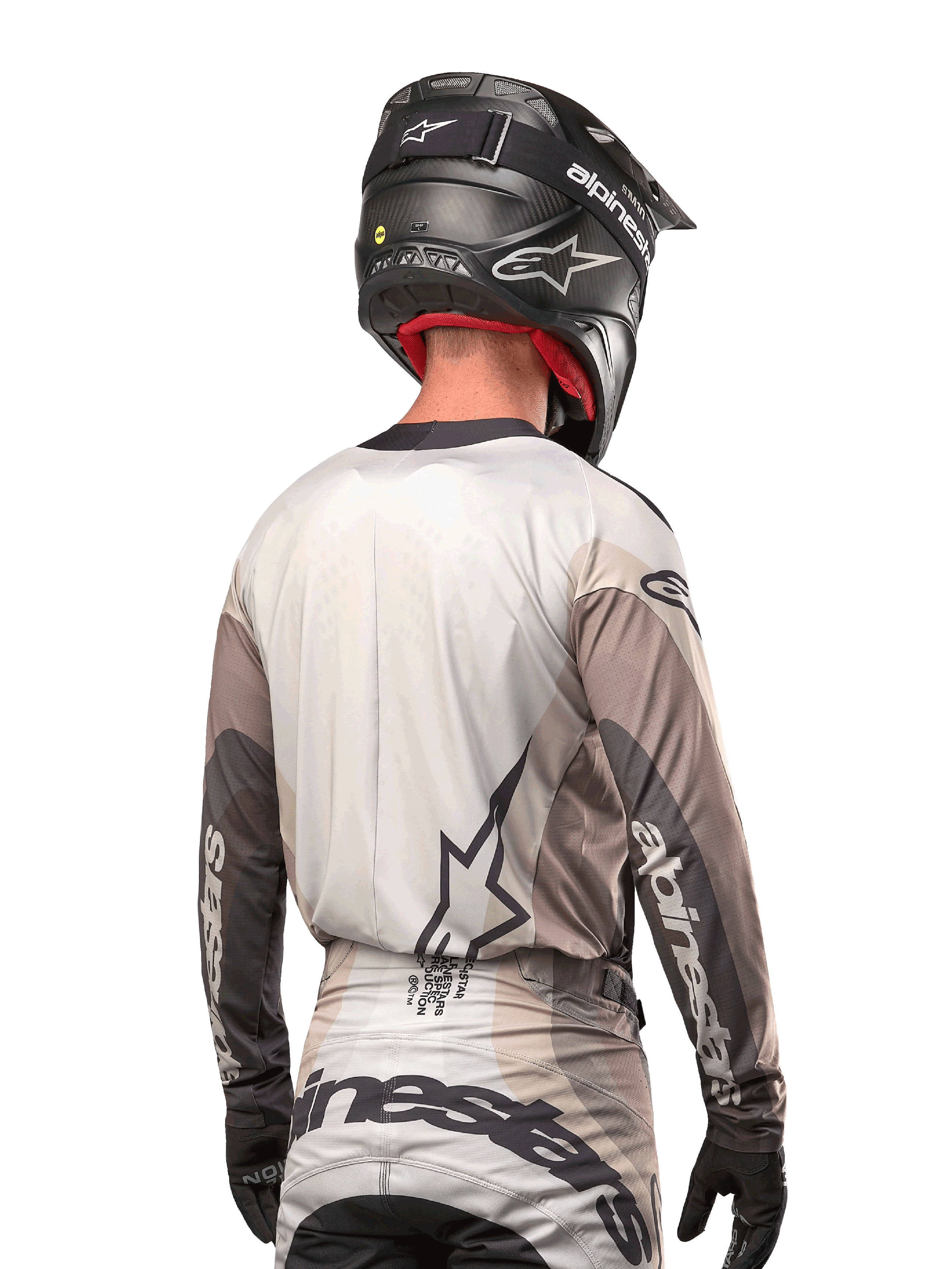 Motocross-rytter set bagfra iført Alpinestars 2024 Techstar Pneuma Jersey i Dark Sand Iron Dust Gray, kombineret med en sort hjelm med carbon-finish, med et stort stjernelogo på ryggen og Alpinestars-branding på ærmerne.