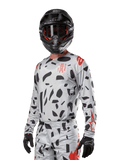 Alpinestars 2024 Techstar Rantera trøje, motocross-trøje, Haze Gray Camo med sorte abstrakte mønstre og røde detaljer, langærmet design båret med matchende sort hjelm og handsker, teknisk off-road racerudstyr
