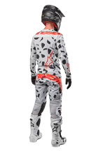 Motocrosskører set bagfra iført Alpinestars 2024 Techstar Rantera bukser, Haze Gray Camo med sorte pletter og røde logoer, matchende trøje, sort hjelm og hvide støvler, komplet off-road racerudstyr