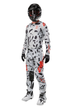 Alpinestars 2024 Techstar Rantera bukser, motocross-bukser, Haze Gray Camo, båret med matchende trøje, sort hjelm og hvide og sorte støvler, med sorte abstrakte mønstre og røde detaljer, komplet terrænkørselsudstyr