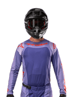 Alpinestars 2024 Techstar Ocuri Jersey, lilla og stærk orange, båret af en motocrosskører med sort hjelm og goggles, med laserskårne perforeringer på brystet, atletisk race-pasform og markant rød branding på skuldrene og brystet.