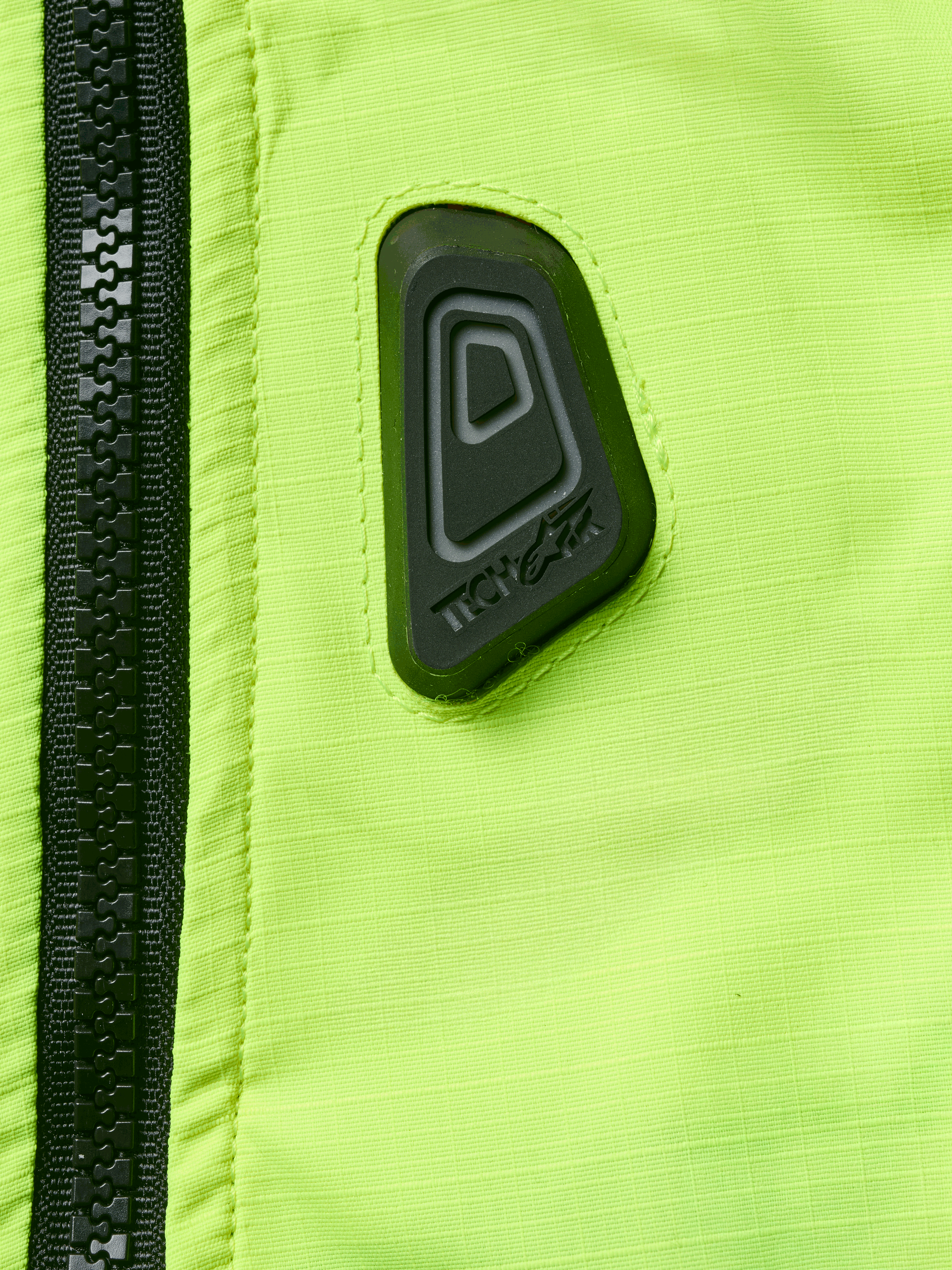 Alpinestars Tech-Air® 3 V2 System, motorcykel-airbagvest, nærbillede af gult fluo vandafvisende stof med sort lynlås, sort gummieret Tech-Air-logomærke, sikkerhedsudstyr med høj synlighed