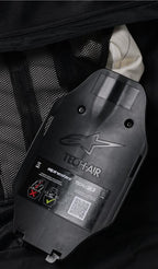 Alpinestars Tech-Air 3 V2 System, indvendig visning af gasinflator- og ECU-huset, sort plast med præget logo, sikkerhedsmærkat med QR-kode og installationsdiagrammer, sort mesh-inderfor, detalje af det brugerservicerbare autonome airbagsystem