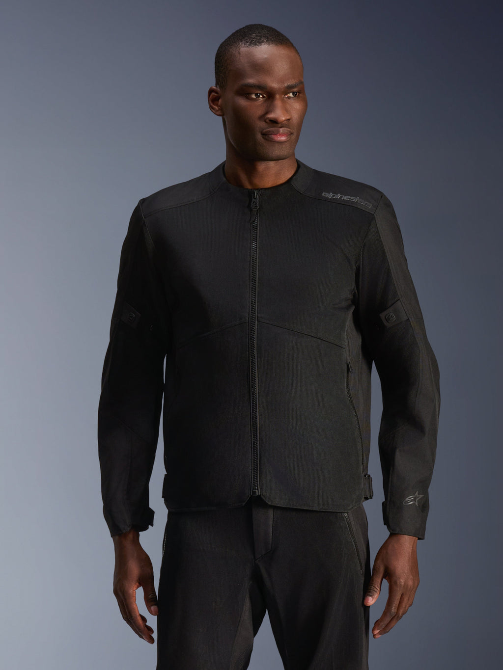 Mandlig model iført Alpinestars C-1 Air-jakke i sort, moderne motorcykeljakke med omfattende tech mesh-paneler og gennemgående lynlås foran, kombineret med matchende sorte kørebukser, æstetik til urban livsstil og pendling